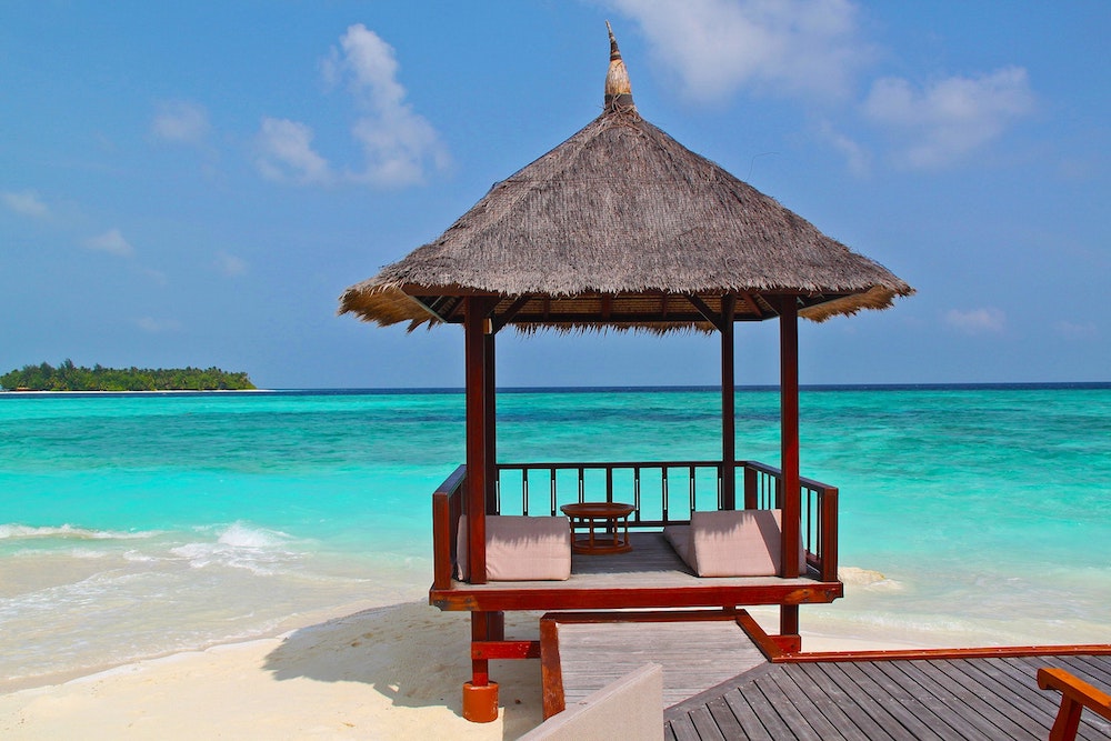 Grass beach hut on the shore of turquoise ocean.